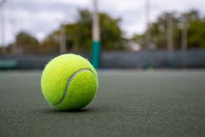Vibrant tennis ball on outdoor court surface, focusing on texture and color.