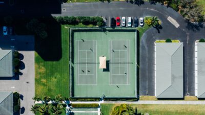 Drone shot showcasing tennis courts, parked cars, and residential area.