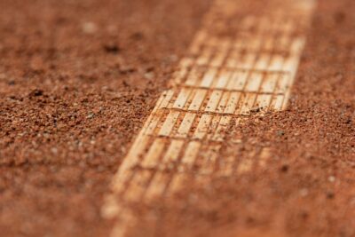Detailed close-up of a red clay tennis court surface with visible court lines.