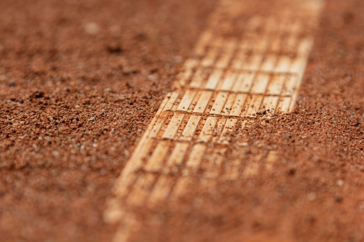 Detailed close-up of a red clay tennis court surface with visible court lines.