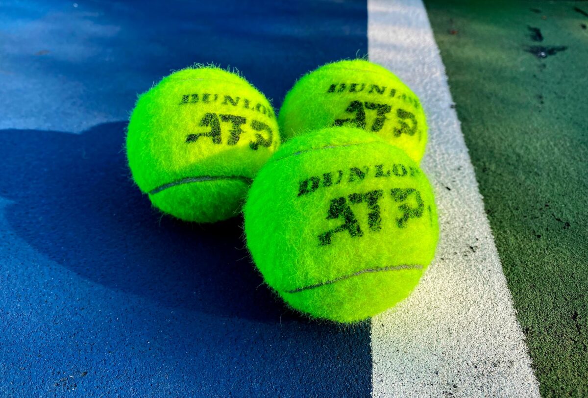 Vivid close-up of three Dunlop ATP tennis balls on a colorful outdoor court.